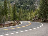 the curved road curves in front of a mountain area with pine trees behind it,