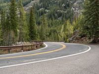 the curved road curves in front of a mountain area with pine trees behind it,