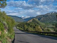 the road winds up on the mountainside on a sunny day with beautiful clouds and trees