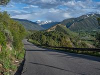 the road winds up on the mountainside on a sunny day with beautiful clouds and trees