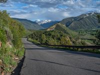 the road winds up on the mountainside on a sunny day with beautiful clouds and trees