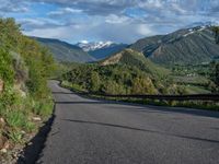 the road winds up on the mountainside on a sunny day with beautiful clouds and trees