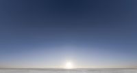 a single skier in a blue sky surrounded by snow on the ground and behind them are some mountains with tall trees