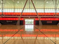 an indoor gym with a basketball net in the floor and red walls and windows on the other side of the room