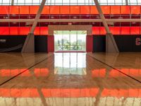 an indoor gym with a basketball net in the floor and red walls and windows on the other side of the room