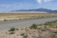 a dirt road and a large mountain range near a desert area, with the side road to the right