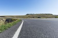 an empty road with a steep hill in the background on a sunny day near the coast