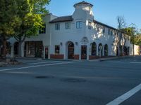 a large white building sitting in the middle of a street with trees surrounding it and an intersection