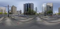 a big street intersection with some trees and tall buildings in the background - looking like a panorama lens