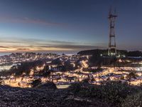 a city with a telephone tower at sunset and lit up at night from the peak