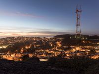 a city with a telephone tower at sunset and lit up at night from the peak