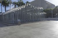 a street scene in a city with light poles and palm trees on the sidewalk and a bench
