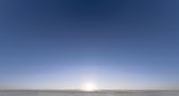 the sun is shining above a barren field of snow covered ground, with a line of trees