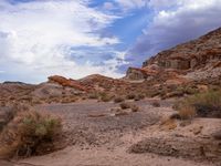 a dirt field surrounded by rocks under a cloudy sky in the desert with shrubs and shrubs around it