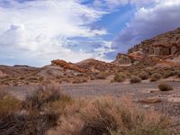 a dirt field surrounded by rocks under a cloudy sky in the desert with shrubs and shrubs around it