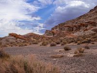 a dirt field surrounded by rocks under a cloudy sky in the desert with shrubs and shrubs around it