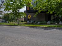 a building with a logo painted on the side near a street that has a sidewalk next to it