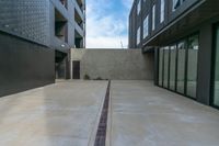 a narrow concrete walkway in a residential building area with multiple glass doors and windows on either side