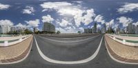 a road and buildings with a cloudy blue sky in the background for a 360 - lens photo