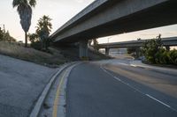 an empty highway under a freeway with some trees in the background and the light from the sky