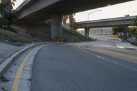 an empty highway under a freeway with some trees in the background and the light from the sky