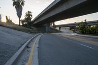 an empty highway under a freeway with some trees in the background and the light from the sky