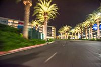 a blurry image of a busy street with some palm trees at night time in an area full of shops