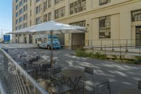 an ice cream truck parked outside a building with tables and umbrellas next to the sidewalk