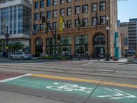 the green paint is painted on a bike path in front of an office building and large, trees