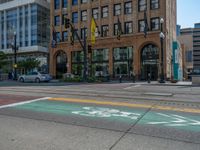 the green paint is painted on a bike path in front of an office building and large, trees