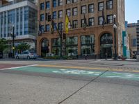 the green paint is painted on a bike path in front of an office building and large, trees