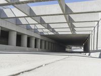 a man riding a skateboard down a concrete walkway with concrete walls behind him and large concrete pillars lining the space