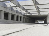 a man riding a skateboard down a concrete walkway with concrete walls behind him and large concrete pillars lining the space