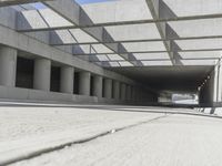 a man riding a skateboard down a concrete walkway with concrete walls behind him and large concrete pillars lining the space