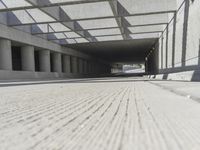 a man riding a skateboard down a concrete walkway with concrete walls behind him and large concrete pillars lining the space