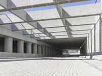 a man riding a skateboard down a concrete walkway with concrete walls behind him and large concrete pillars lining the space