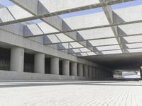 a man riding a skateboard down a concrete walkway with concrete walls behind him and large concrete pillars lining the space