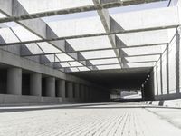 a man riding a skateboard down a concrete walkway with concrete walls behind him and large concrete pillars lining the space