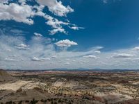 a vast mountainous landscape with blue skies above the tops and some brown dirt fields below