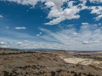 a vast mountainous landscape with blue skies above the tops and some brown dirt fields below