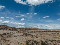 a vast mountainous landscape with blue skies above the tops and some brown dirt fields below