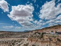 a vast mountainous landscape with blue skies above the tops and some brown dirt fields below