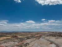 a vast mountainous landscape with blue skies above the tops and some brown dirt fields below