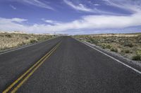 a lone road stretches out into the distance in the desert under a blue sky with white clouds