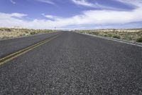 a lone road stretches out into the distance in the desert under a blue sky with white clouds