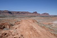 a dirt road through a desert plain with a mountain behind it and a clear blue sky in the background