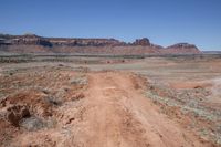 a dirt road through a desert plain with a mountain behind it and a clear blue sky in the background