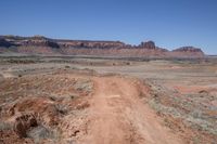 a dirt road through a desert plain with a mountain behind it and a clear blue sky in the background