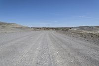 a dirt road is surrounded by some hills and desert like terrain as the vehicle sits on it