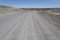 a dirt road is surrounded by some hills and desert like terrain as the vehicle sits on it